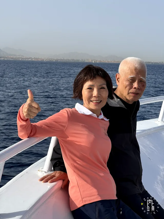爸爸和媽媽在船頭靠近鏡頭,風把衣角吹起來,人仍然笑得很穩